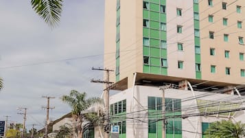 Un edificio de varios pisos con un diseño arquitectónico moderno, que destaca por su fachada verde y numerosos ventanales.
