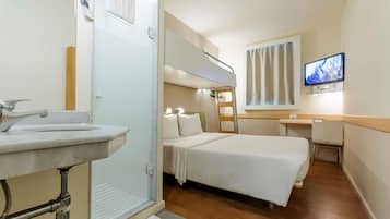 Habitación de hotel pequeña con literas, un escritorio, televisión y baño con lavabo y ducha.