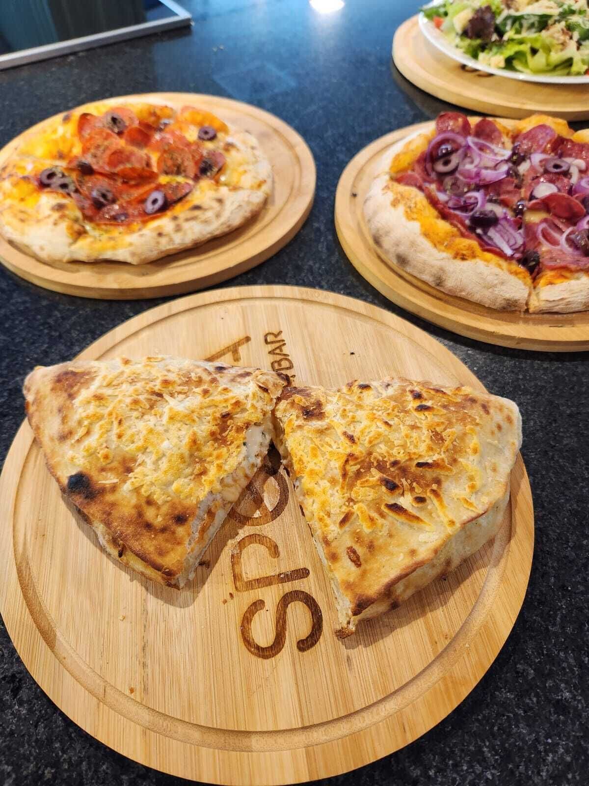 Three pizzas on wooden boards with a kitchen counter in the background.