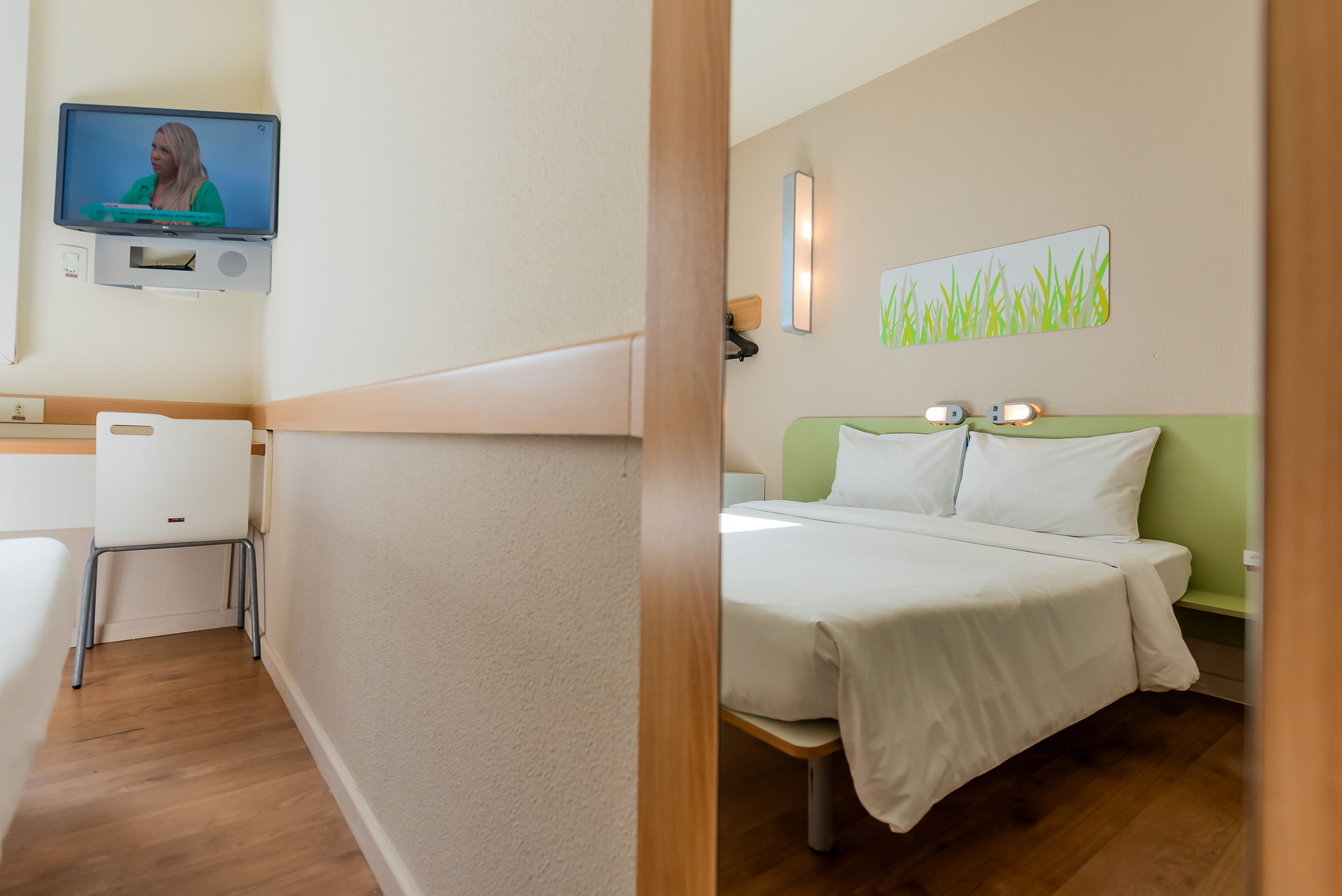 A hotel room with a bed, a desk, and a television mounted on the wall.