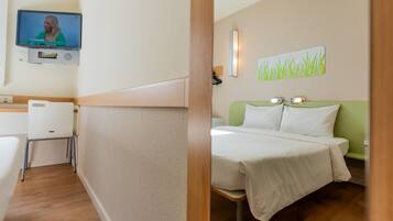 A hotel room with a bed, a desk, and a television mounted on the wall.