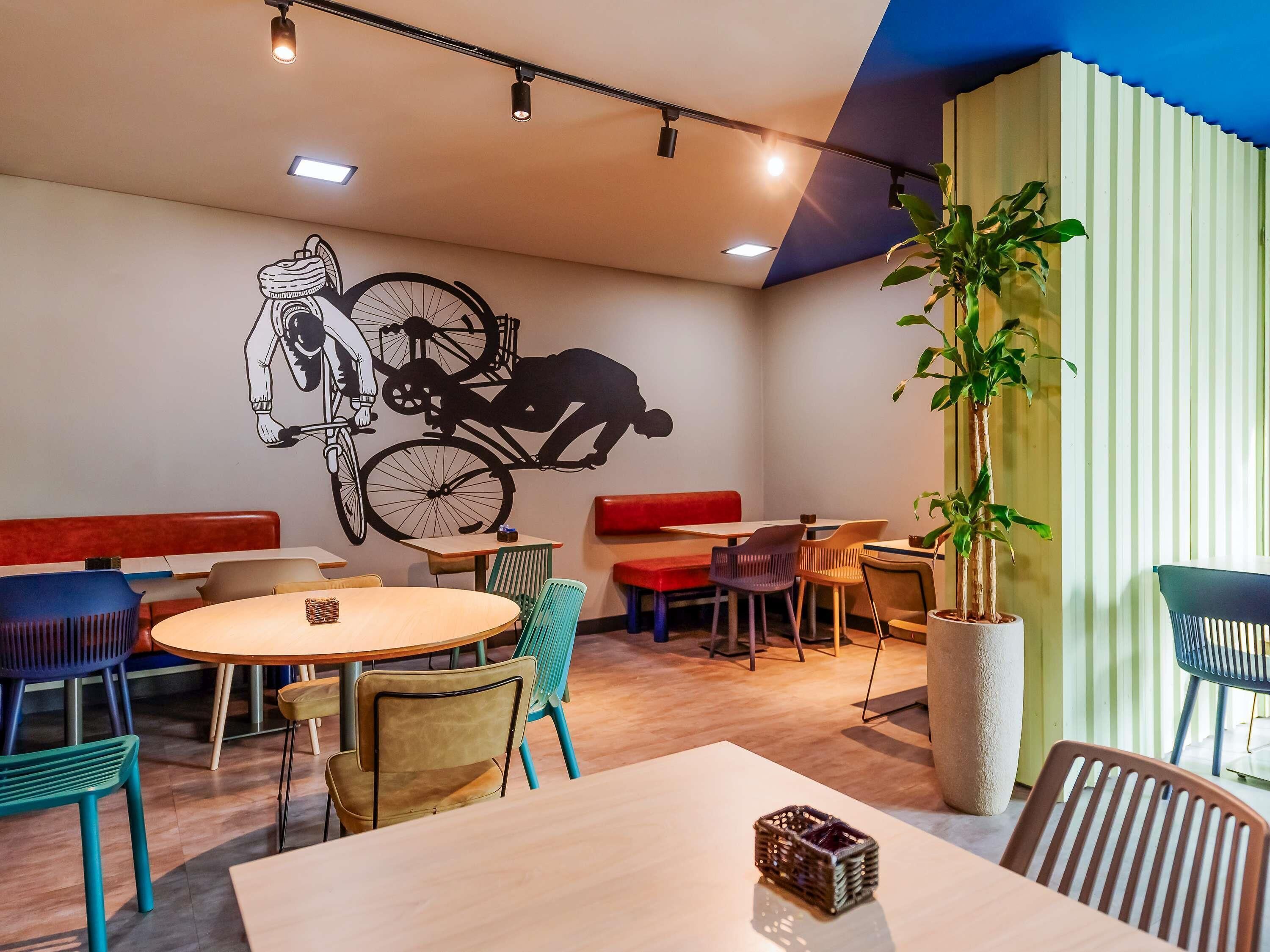 Interior de restaurante con un mural, disposición de los asientos y una planta en maceta.