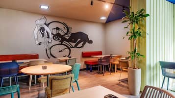 Interior de restaurante con un mural, disposición de los asientos y una planta en maceta.
