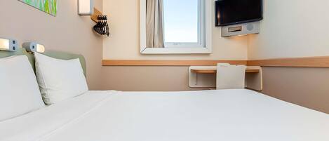 Ett hotellrum med en säng, ett skrivbord, en tv och ett fönster med gardiner.