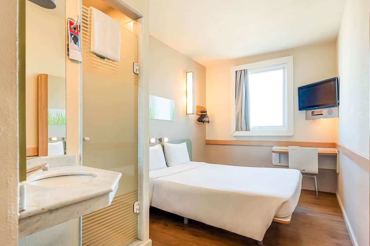 A hotel room with a bed, a desk, a television, and a bathroom with a sink and mirror.