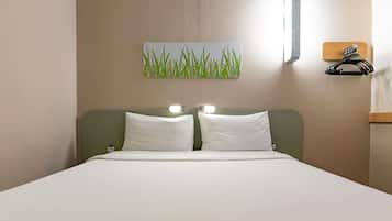 A hotel room with a bed, two pillows, a wall-mounted light, and a painting of grass.