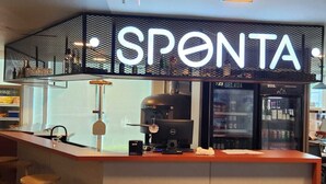 Un espace bar moderne avec un panneau néon sur lequel on peut lire « SPONTA  » et une machine à café.
