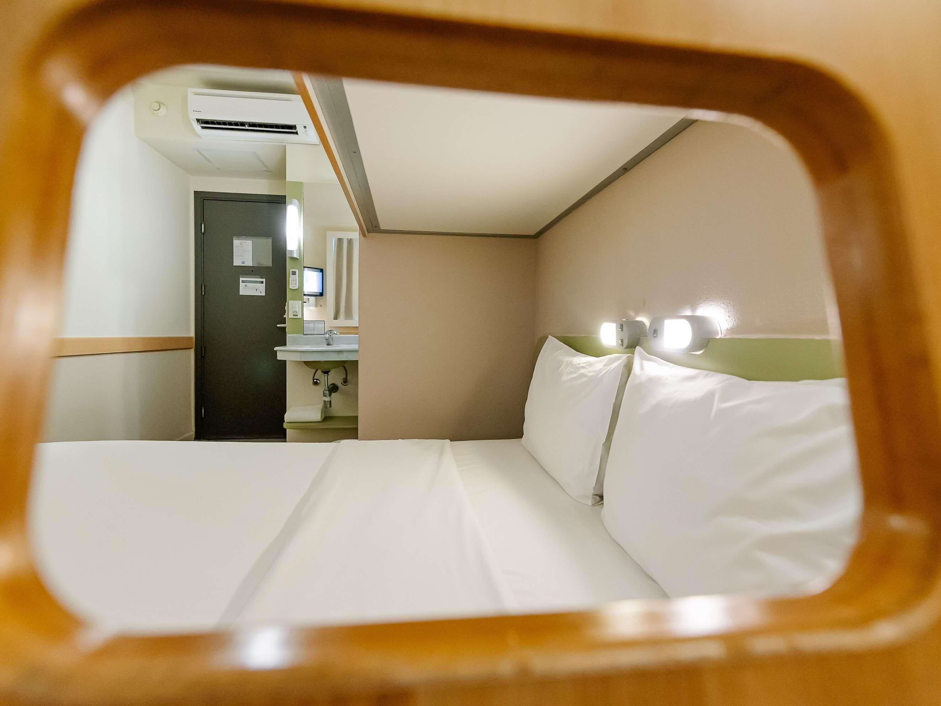 A hotel room with a bed, a sink, a mirror, and an air conditioning unit.