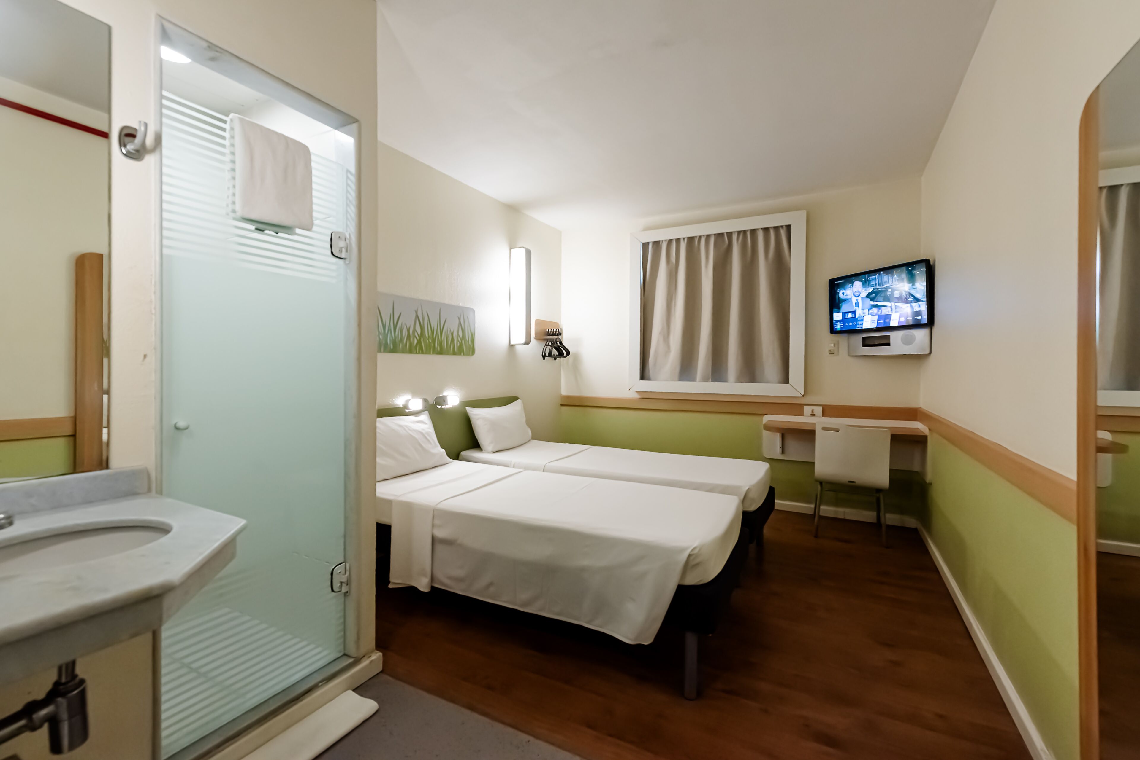 A hotel room with a shower, two beds, a TV, and a desk.