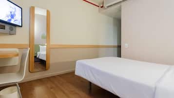 Una habitación de hotel con una cama individual, un escritorio, una silla, un televisor y un equipo de aire acondicionado.