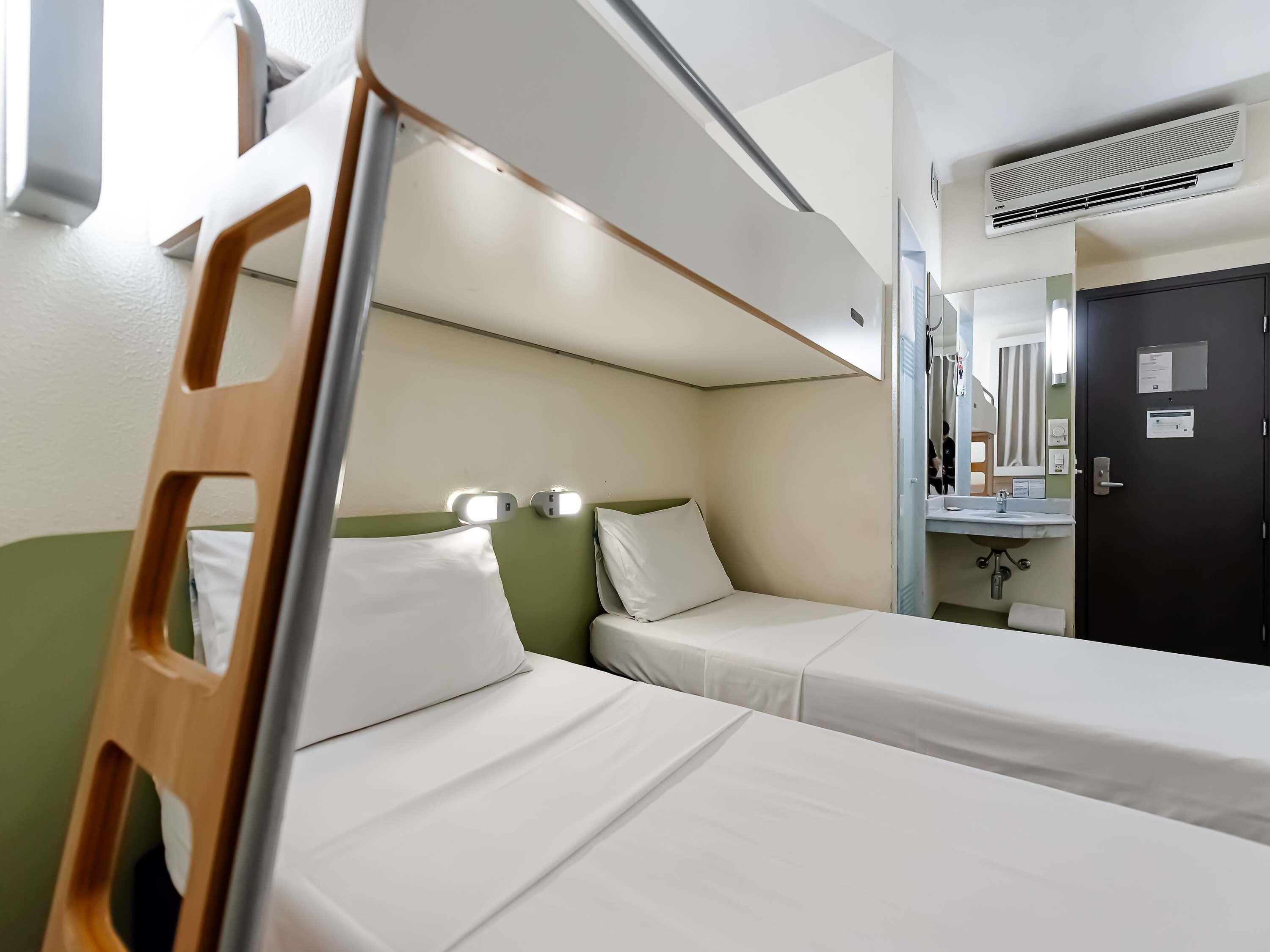 A bunk bed room with a ladder, a bedside table, a mirror, and a door.