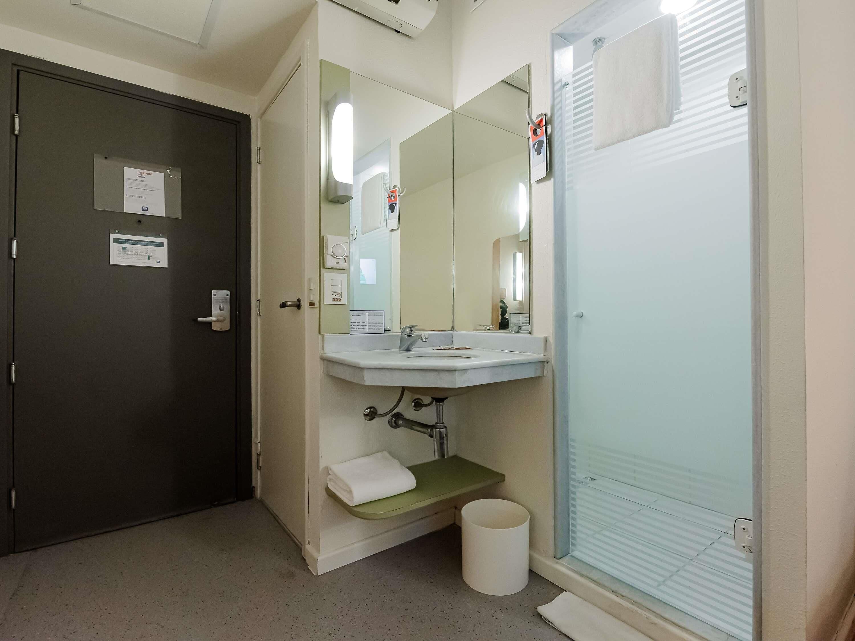 Un baño con lavamanos, espejo, toallero y una puerta con cerradura.