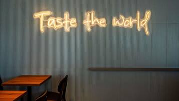 Interior de un restaurante con un letrero de neón que dice 'Taste the world' en la pared.