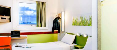Une chambre d’hôtel avec un lit, un bureau avec un ordinateur portable, une télévision et une fenêtre avec des rideaux.