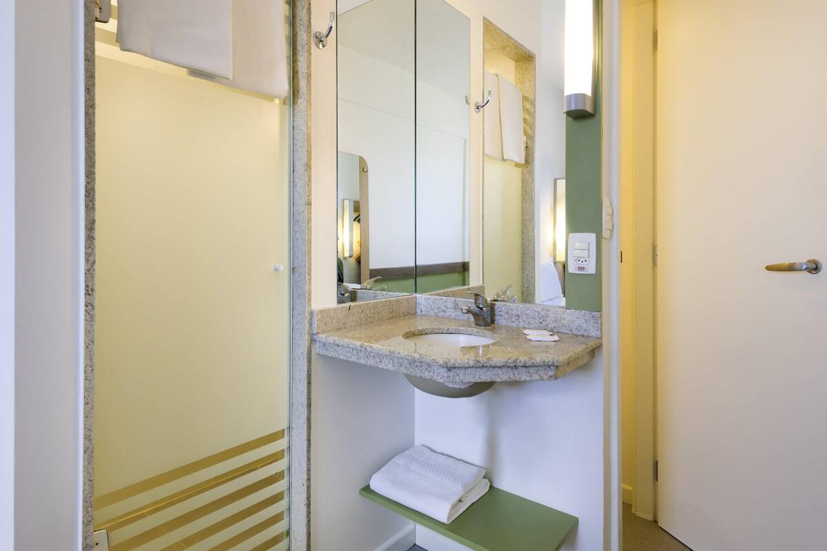 A bathroom with a granite countertop sink, a mirror, a towel rack, and a green shelf.
