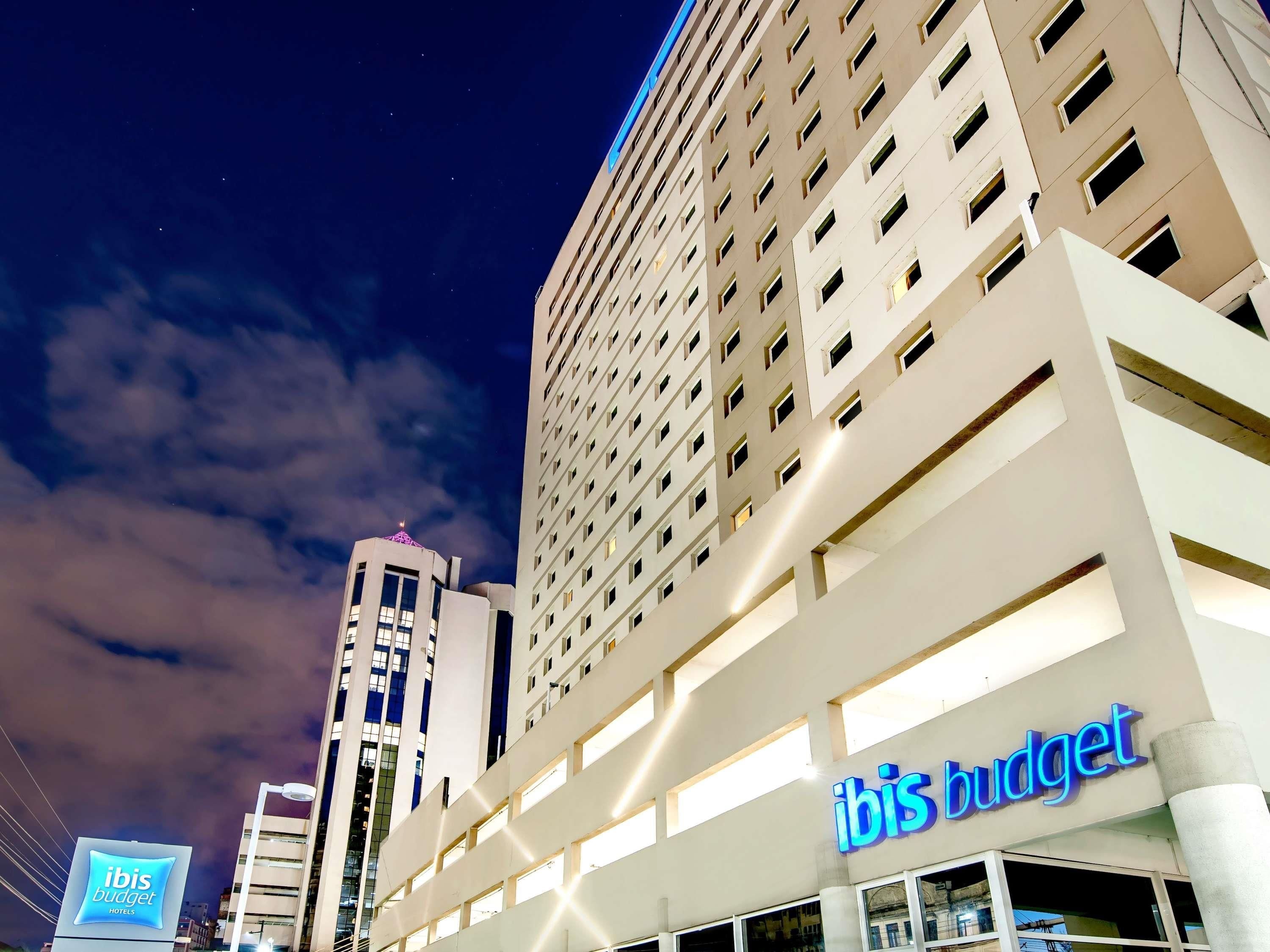 Um hotel com fachada moderna, vários andares e placa chamativa com a inscrição 'ibis budget hotels'.