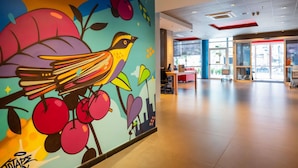 A modern interior with a colorful mural of a bird and fruit, a reception desk, and a glass door entrance. - ibis budget Porto Alegre - Supereconômico (Porto Alegre)
