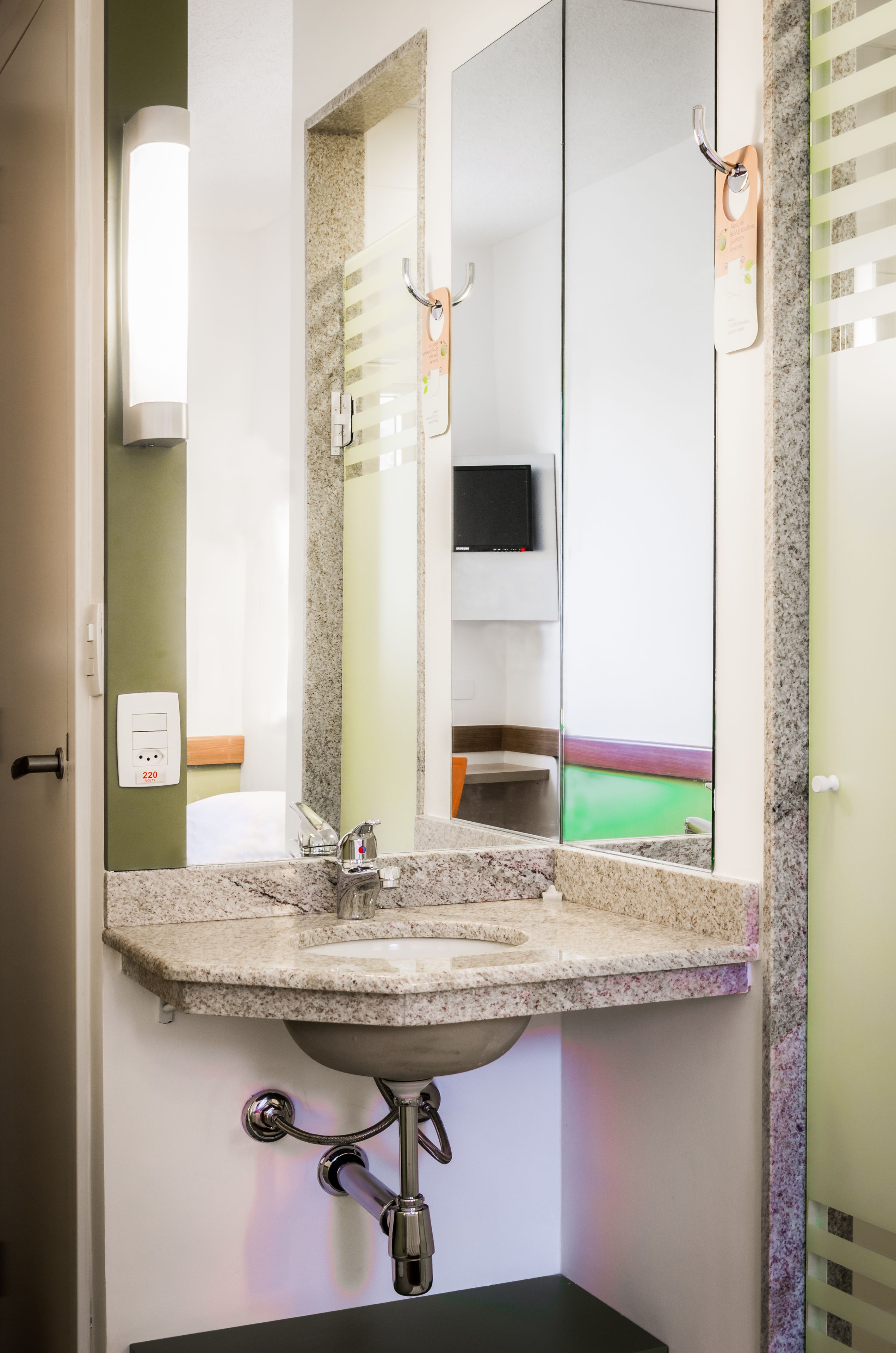 A bathroom with a granite countertop sink, a mirror, a wall-mounted TV, and a towel rack.