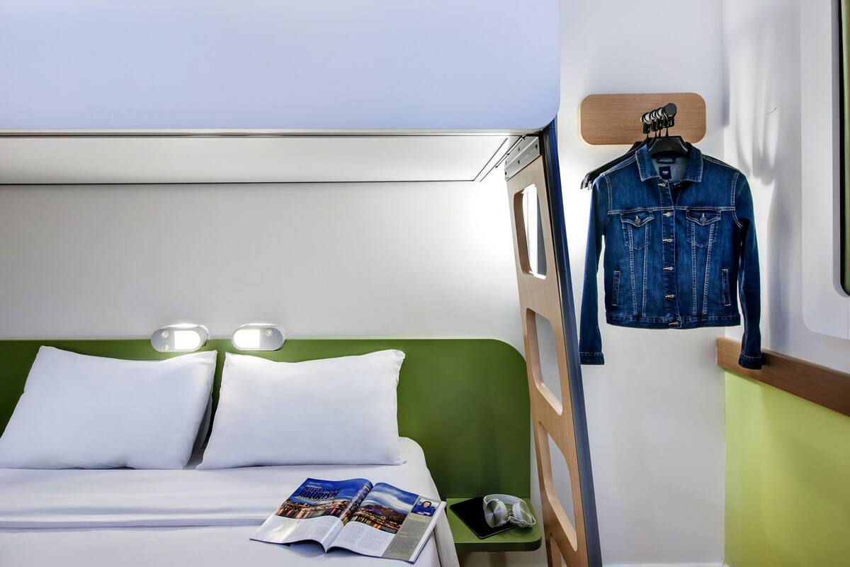 A bunk bed with a green headboard, a white pillow, and a magazine on the bed.