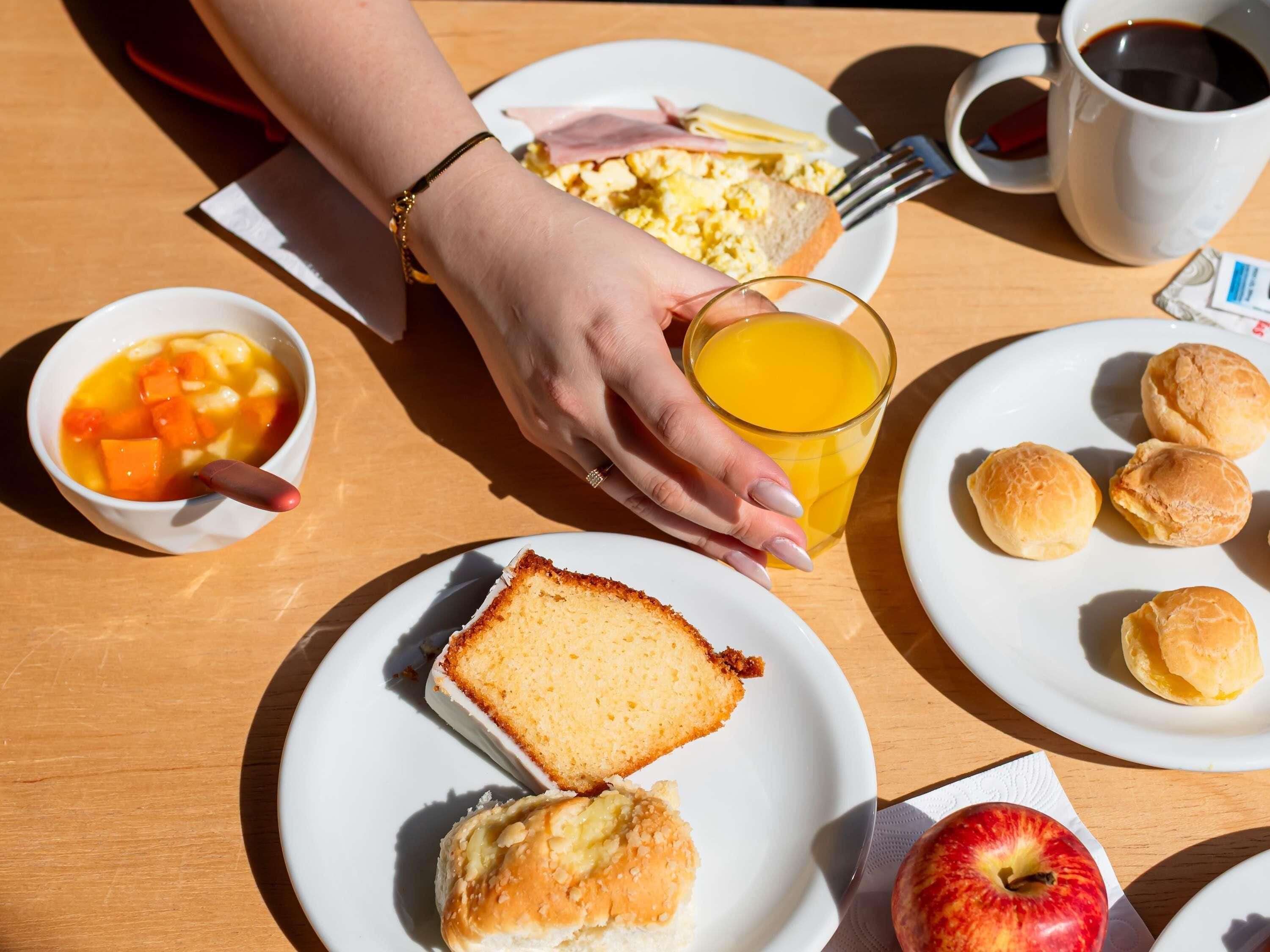 A breakfast setting with a plate of eggs, ham, cheese, toast, biscuits, a glass of orange juice, a bowl of fruit, and a cup of coffee.