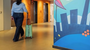 A woman walking with a suitcase in a hallway with elevators and a mural on the wall. - ibis budget Porto Alegre - Supereconômico (Porto Alegre)