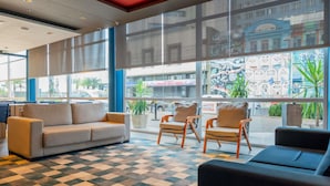 A lobby with a checkered floor, a sofa, two armchairs, and large windows with a view of the street. - ibis budget Porto Alegre - Supereconômico (Porto Alegre)