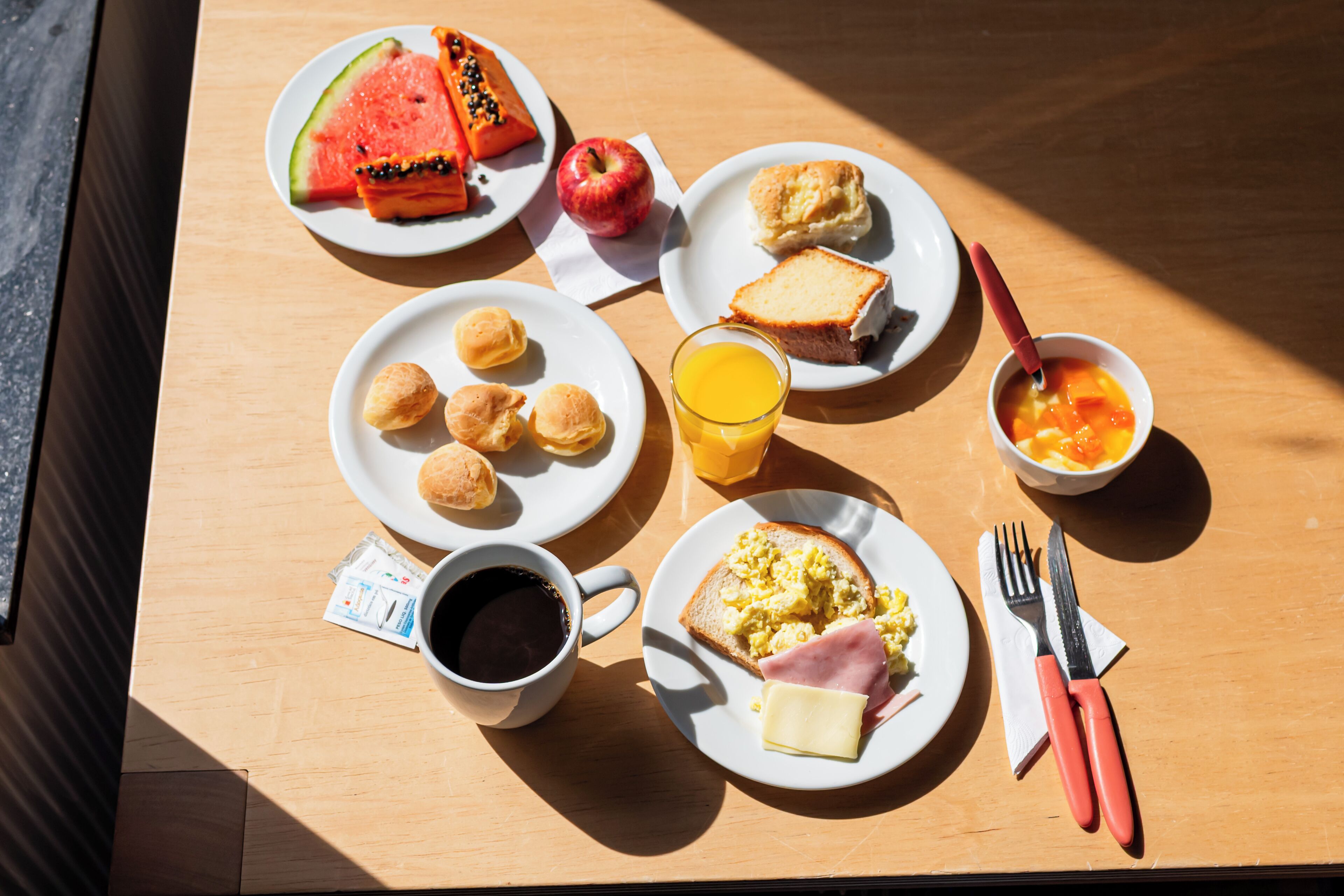 A breakfast table with plates of food, including toast, eggs, ham, and a bowl of fruit.