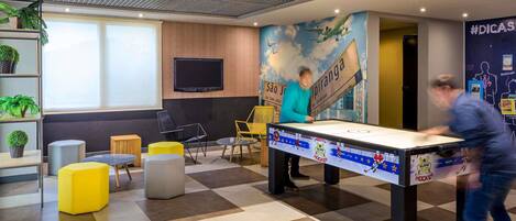 A modern indoor space with a foosball table, seating areas, and a mural.