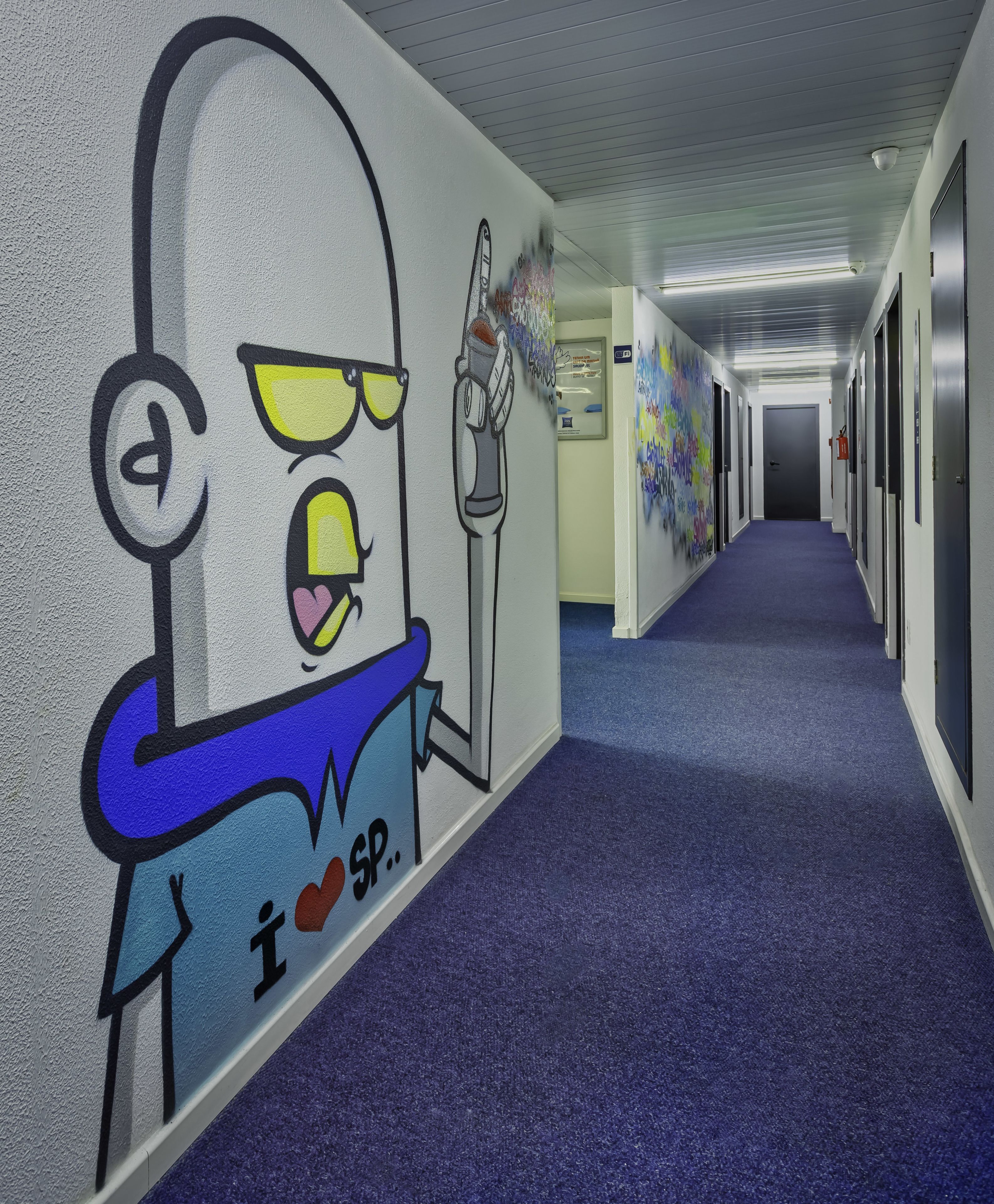 A hallway with a mural of a cartoon character, blue carpet, and doors on both sides.