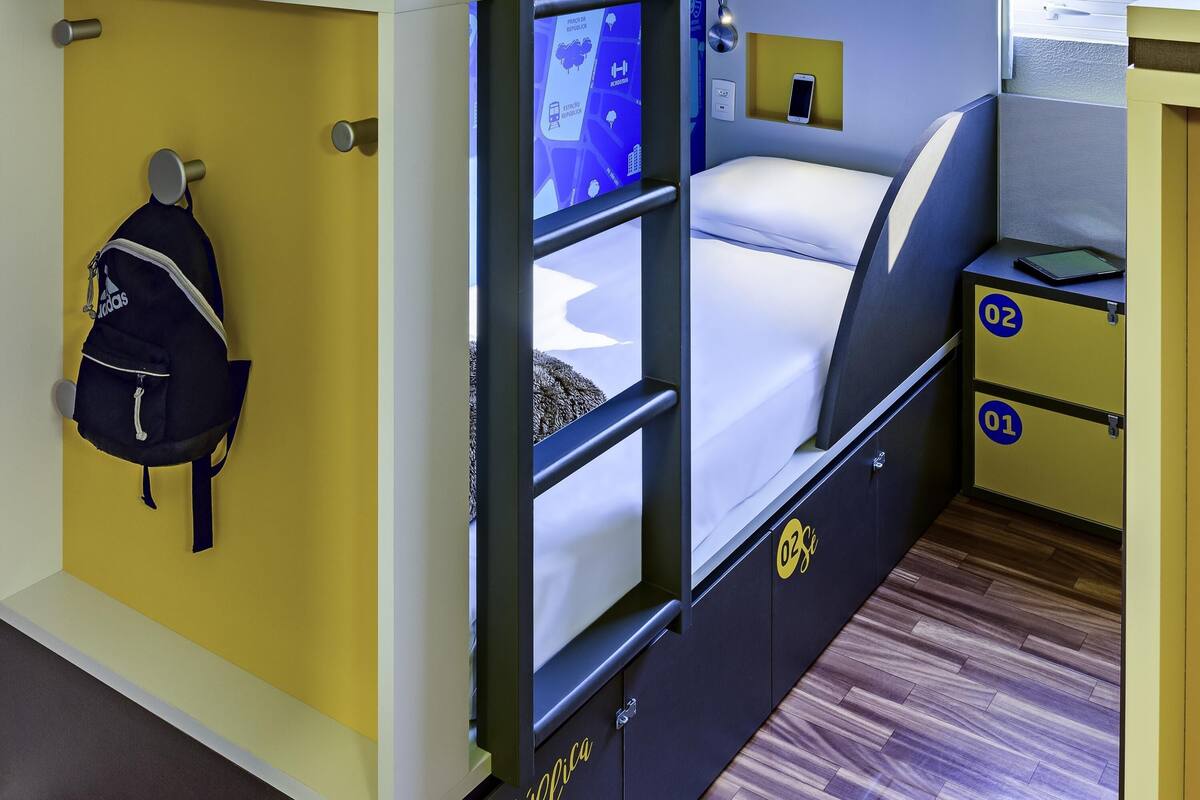 Une chambre d’hôtel de taille réduite, comprenant un lit, un petit bureau, une chaise, une armoire et un téléviseur fixé au mur.