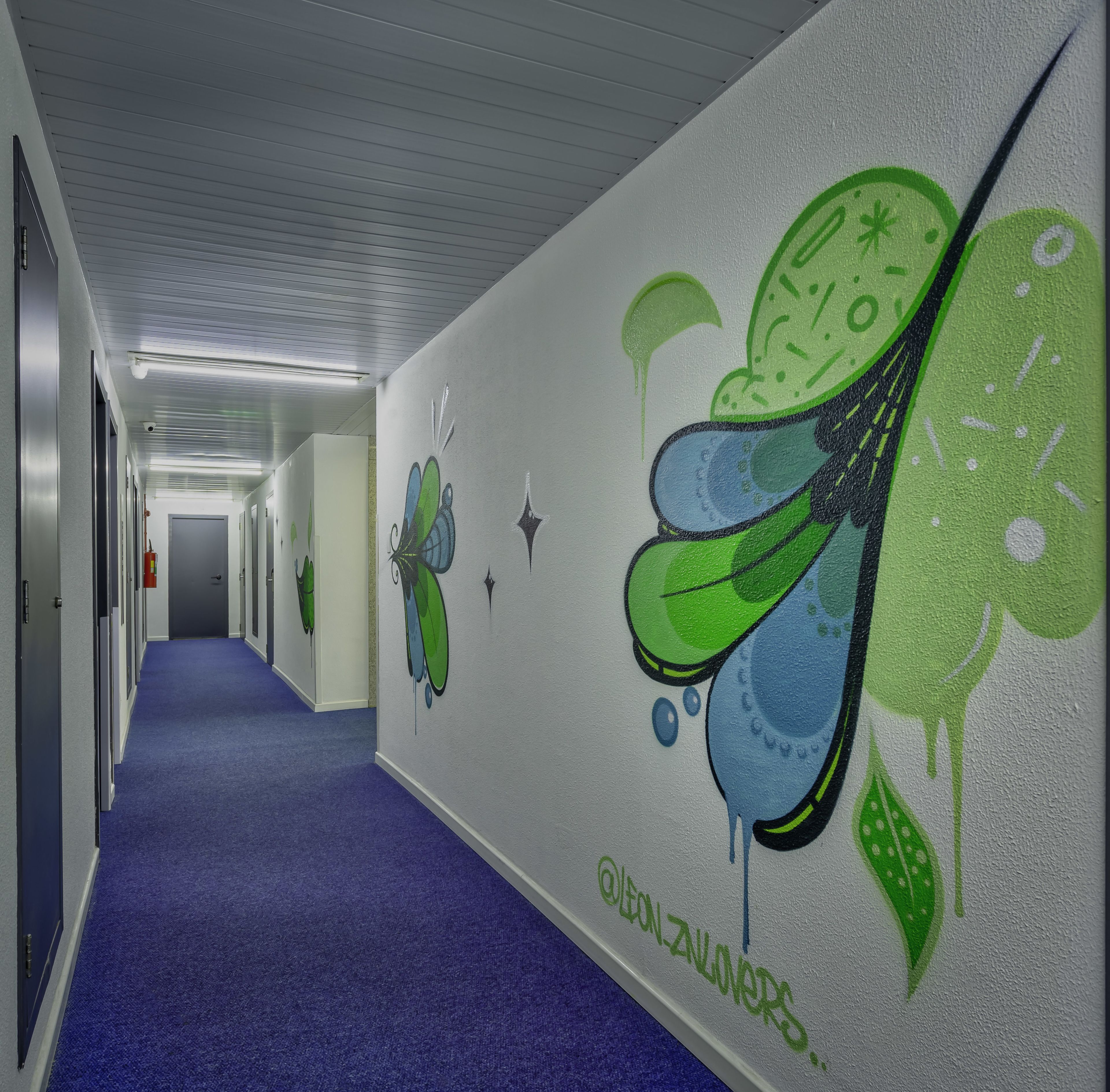 Un pasillo con alfombra azul, paredes blancas y un mural de una mariposa.