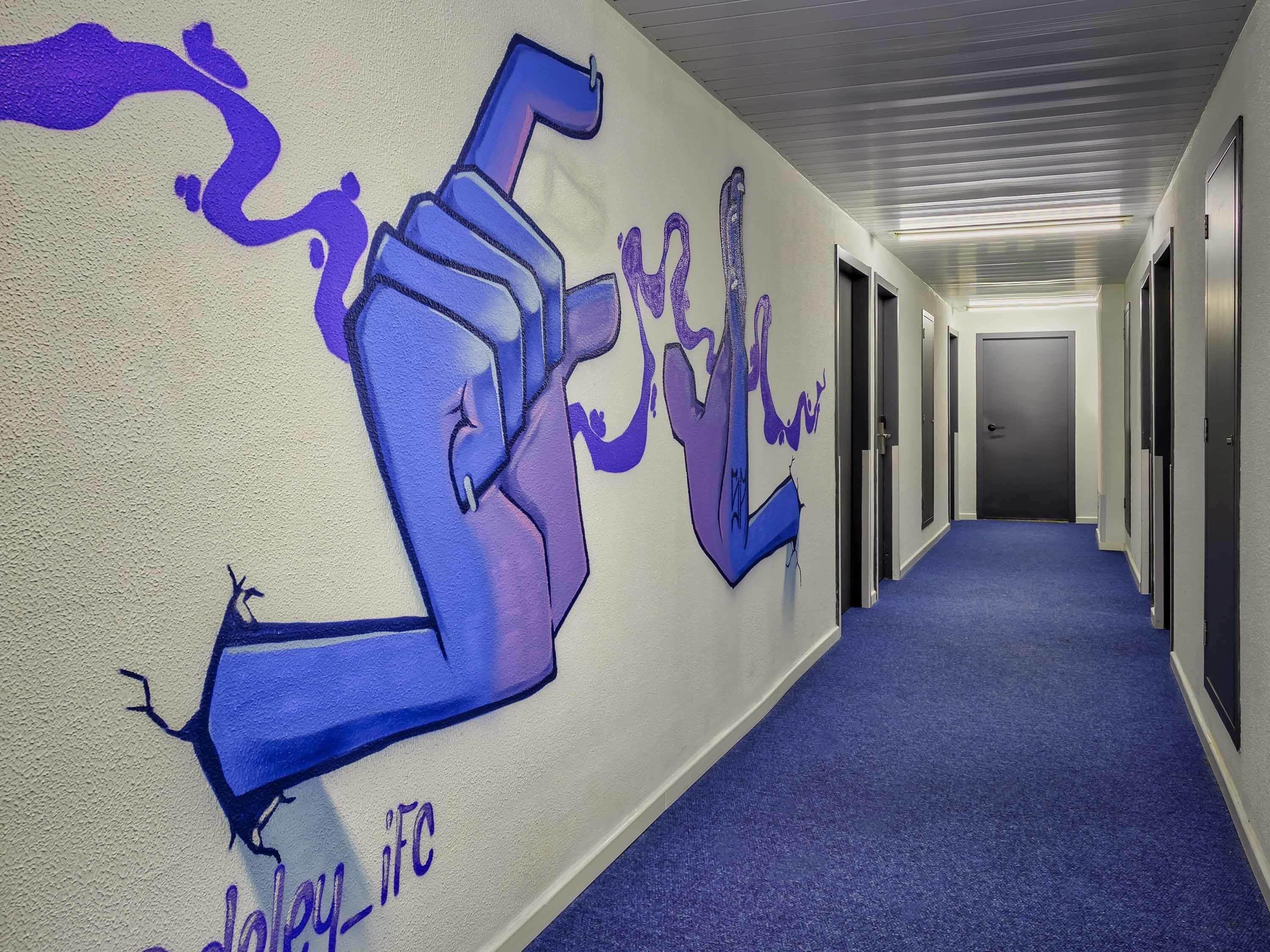 Un pasillo con alfombra azul, un mural en la pared y puertas que dan a habitaciones.