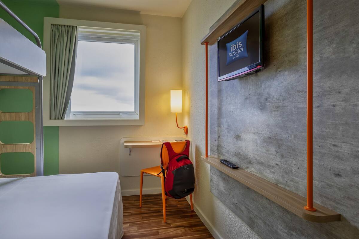 Une chambre d’hôtel équipée d’un lit, d’un bureau, d’une chaise, d’une télévision et d’une fenêtre avec des rideaux.