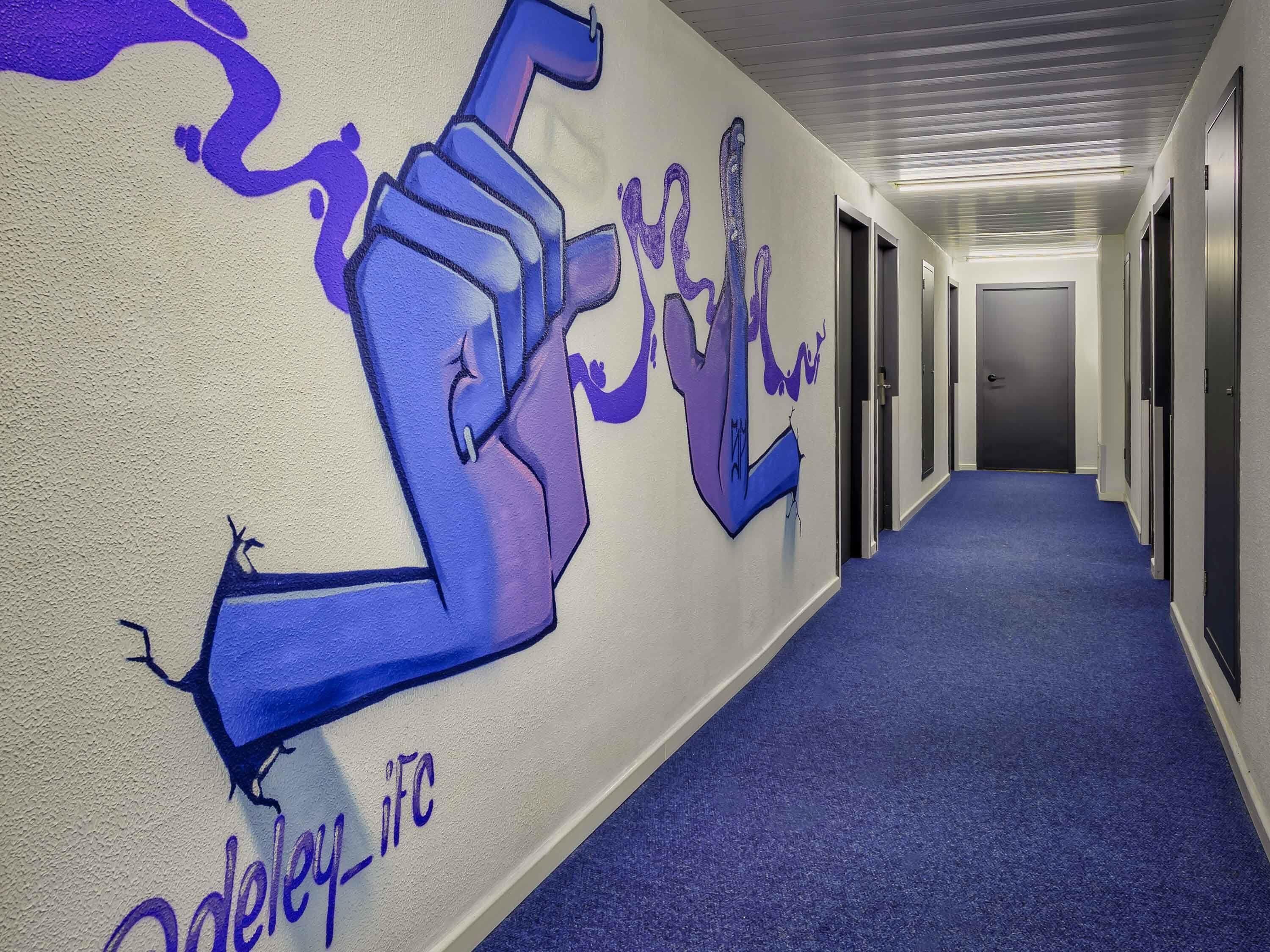 A hallway with a blue carpet, a wall mural, and doors on the right.