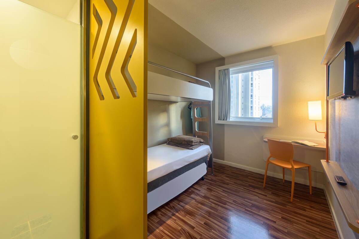 Une petite pièce comprenant un lit superposé, un bureau et une chaise.