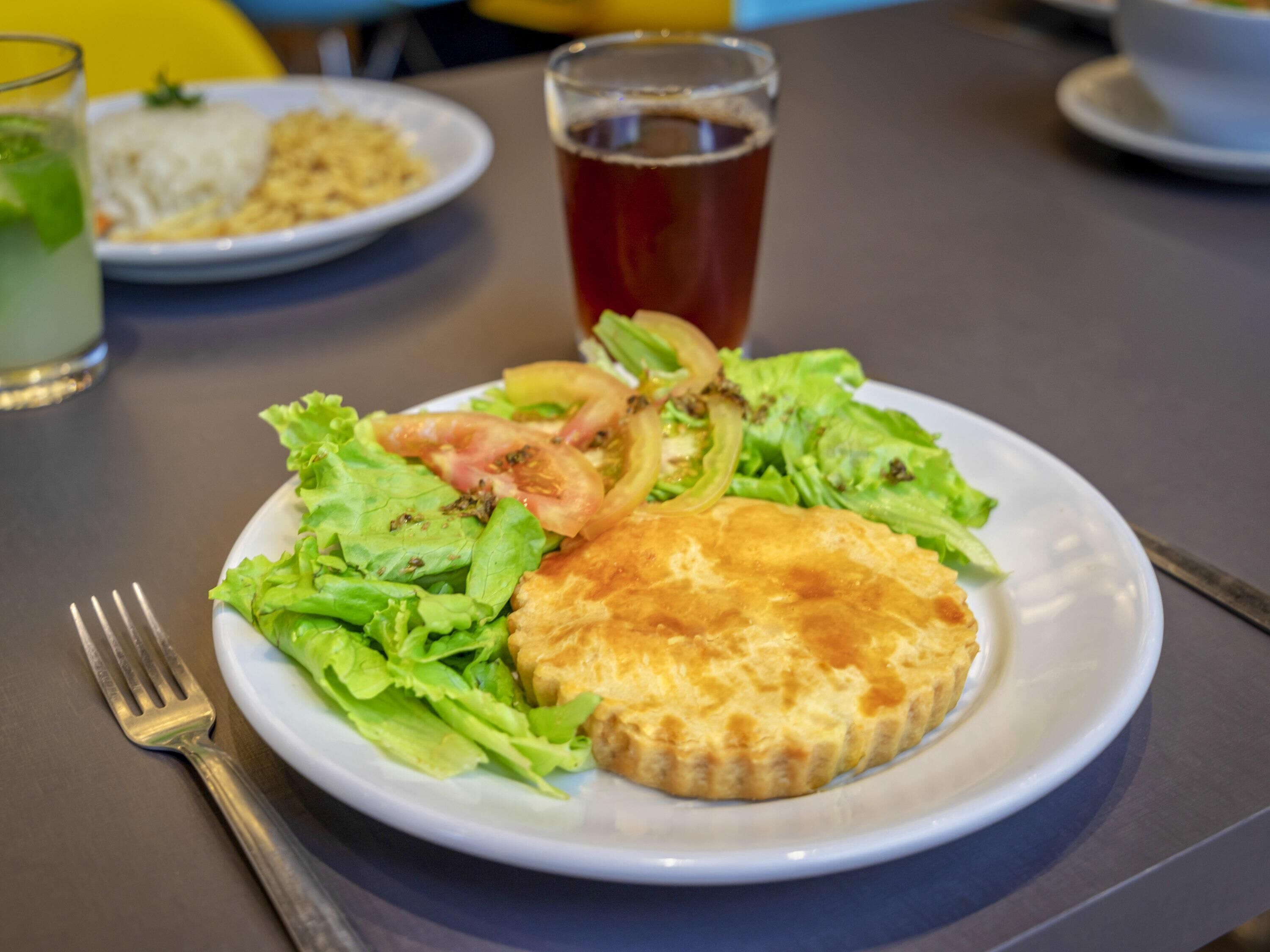 Une assiette contenant une quiche, une salade et un verre de thé, posée sur une table.