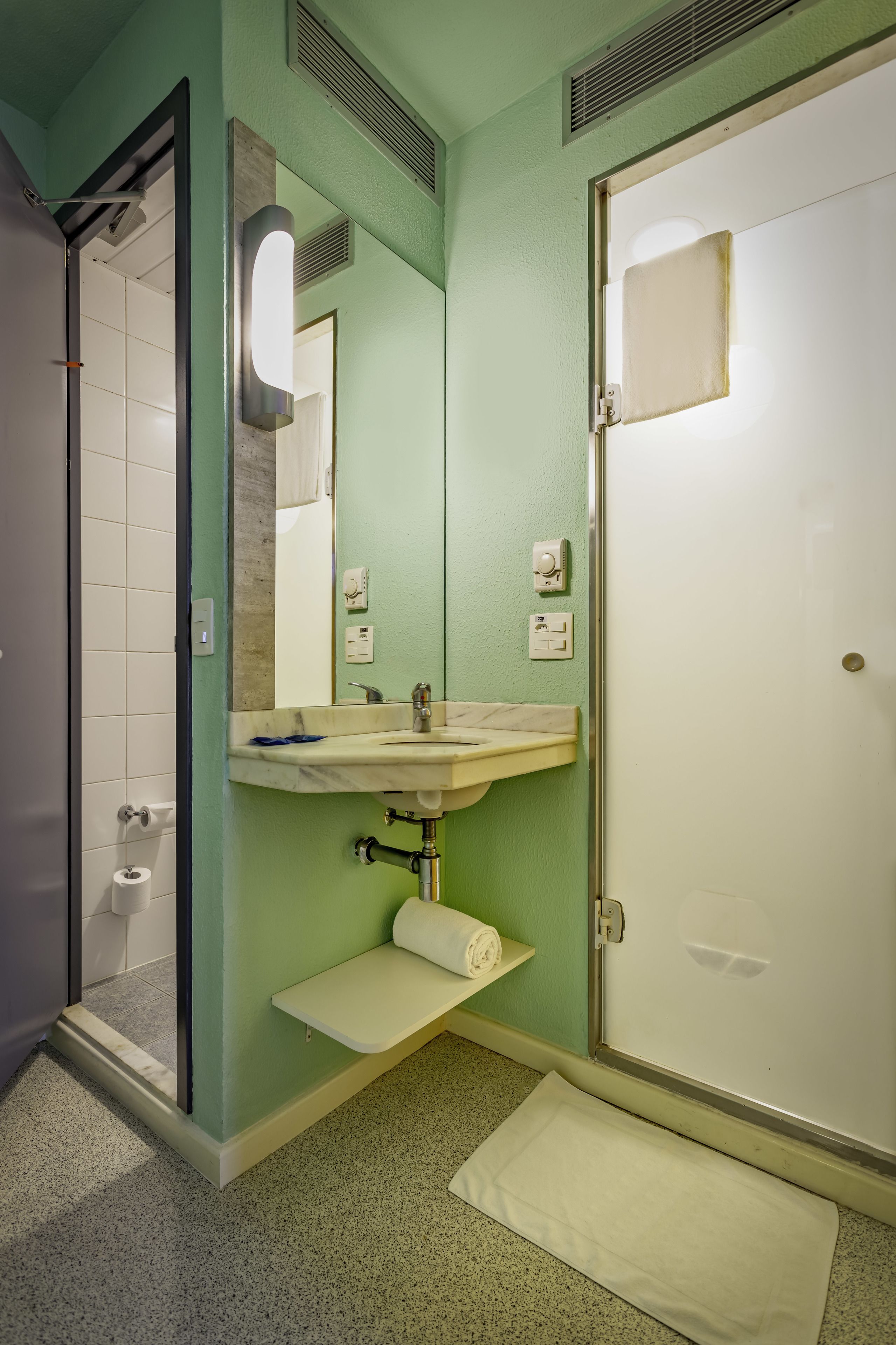 Une salle de bain avec un mur vert, un lavabo blanc, un miroir, un porte-serviettes et une porte de douche.