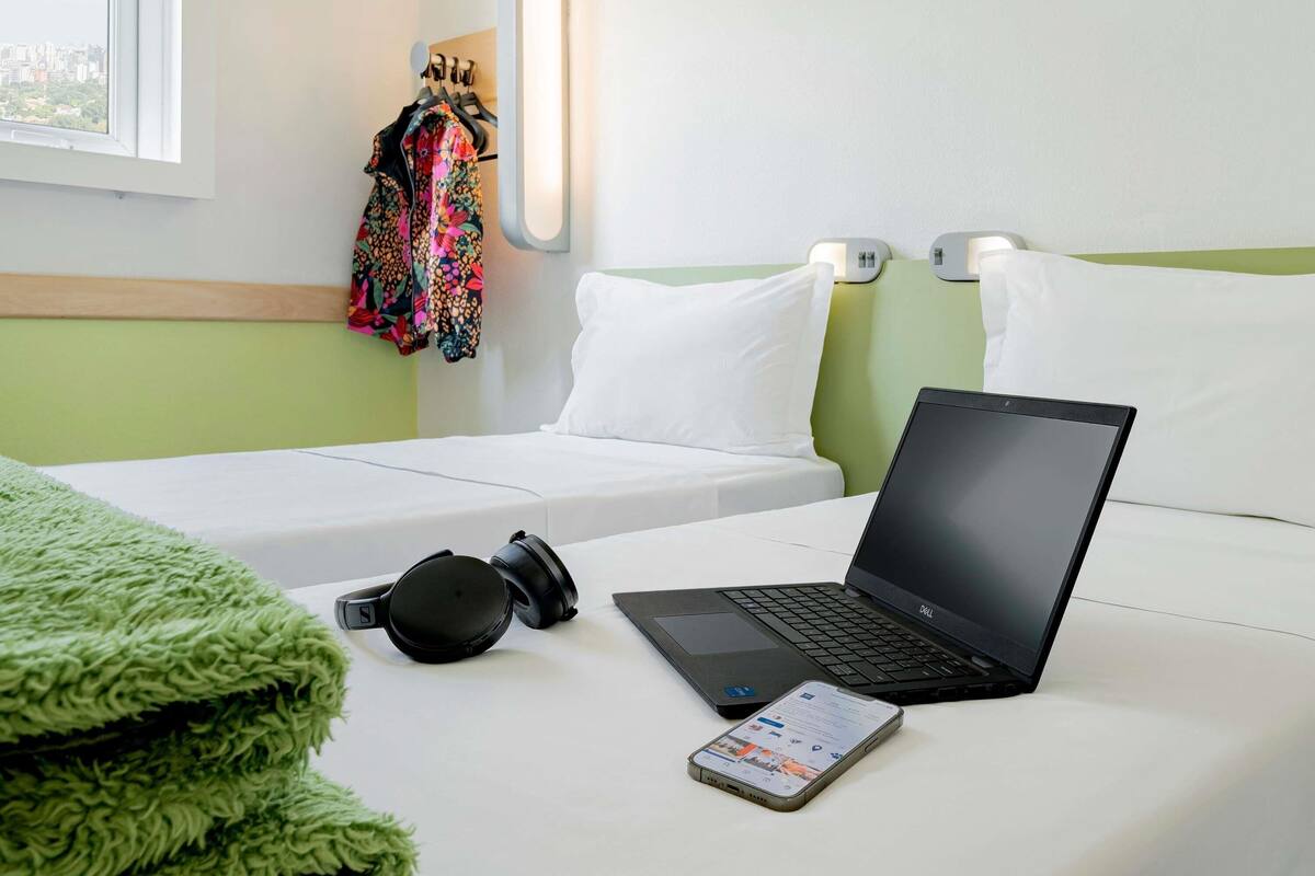 Una habitación de hotel con una cama, una laptop, auriculares y un teléfono inteligente sobre la cama.