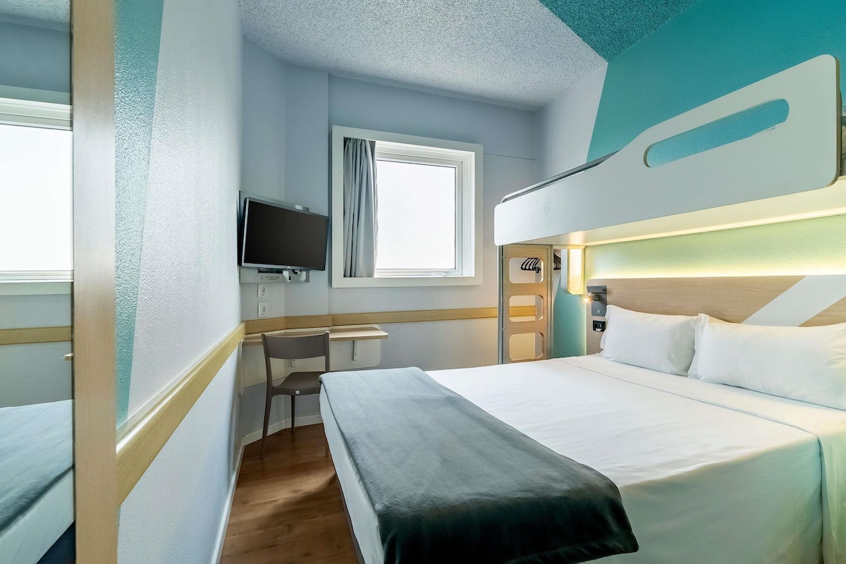 A hotel room with a bed, a desk, a television, and a window.