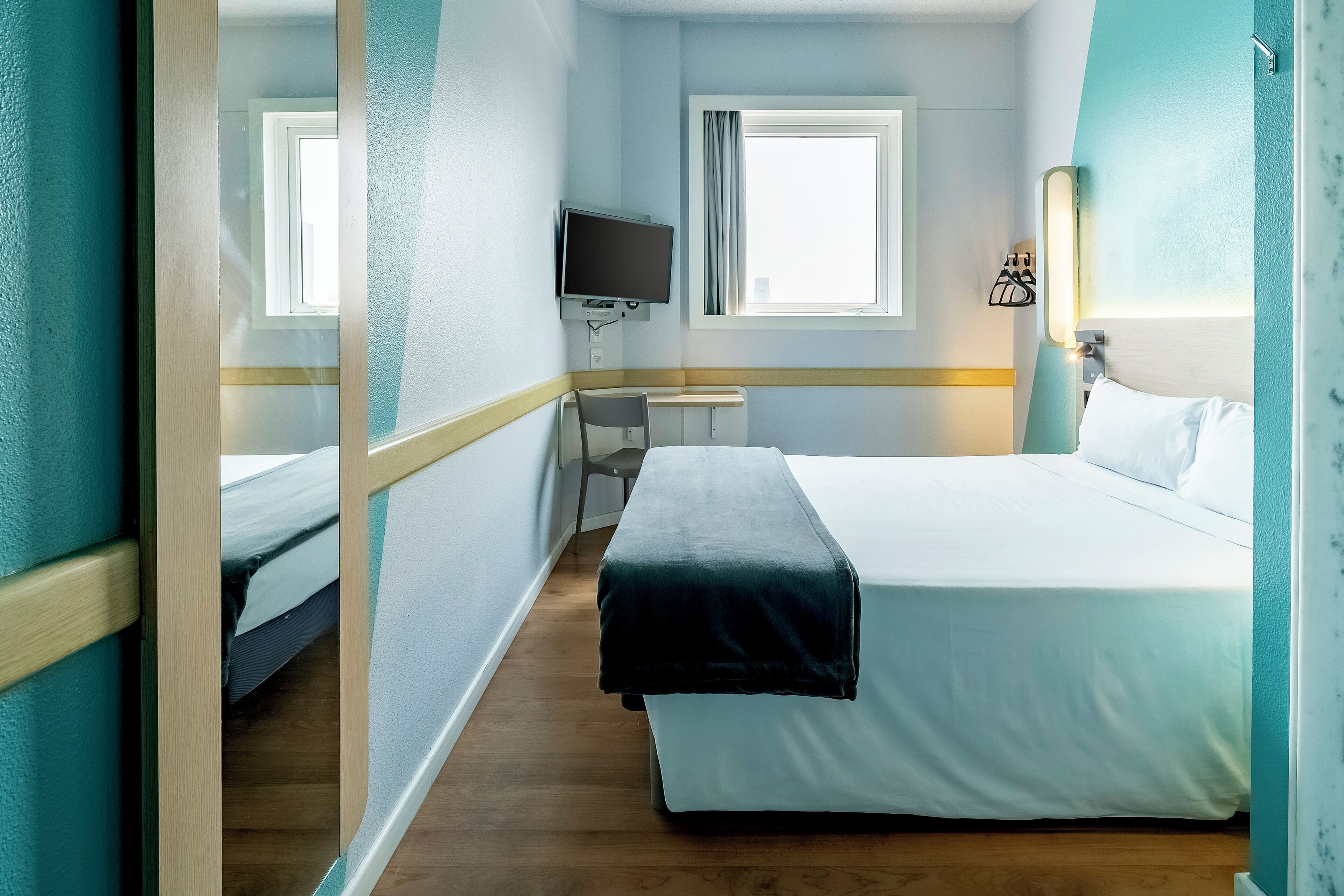 Une chambre d’hôtel avec un lit, un bureau, une chaise, une télévision et une fenêtre.