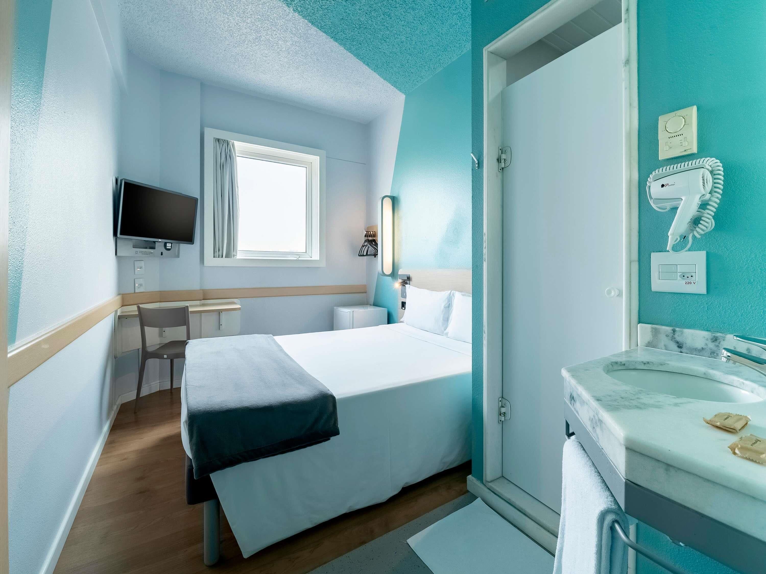 A hotel room with a bed, desk, TV, and bathroom.