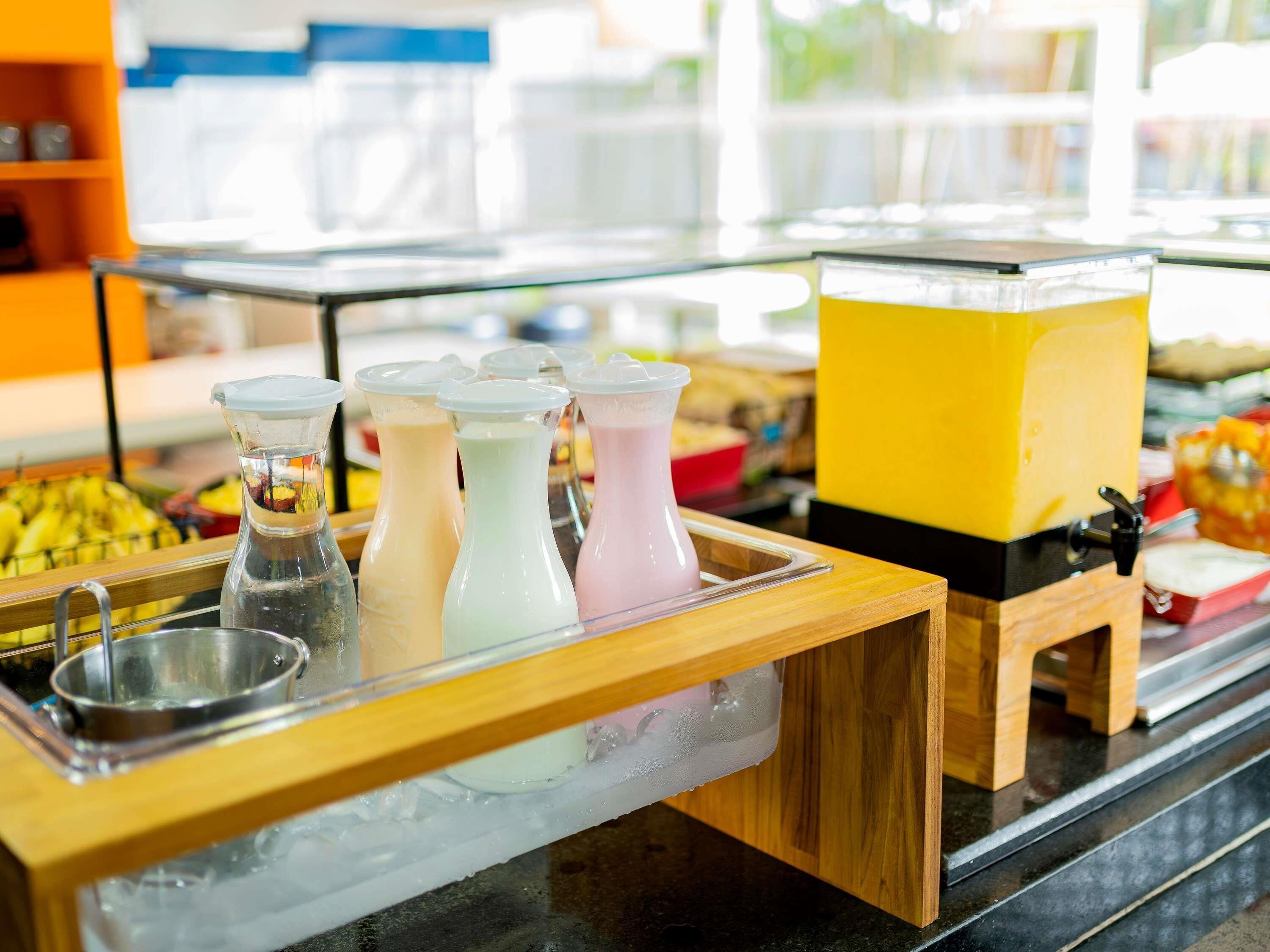 A beverage station with dispensers and a large yellow container, likely for smoothies or shakes, with a metal sink and a wooden counter.