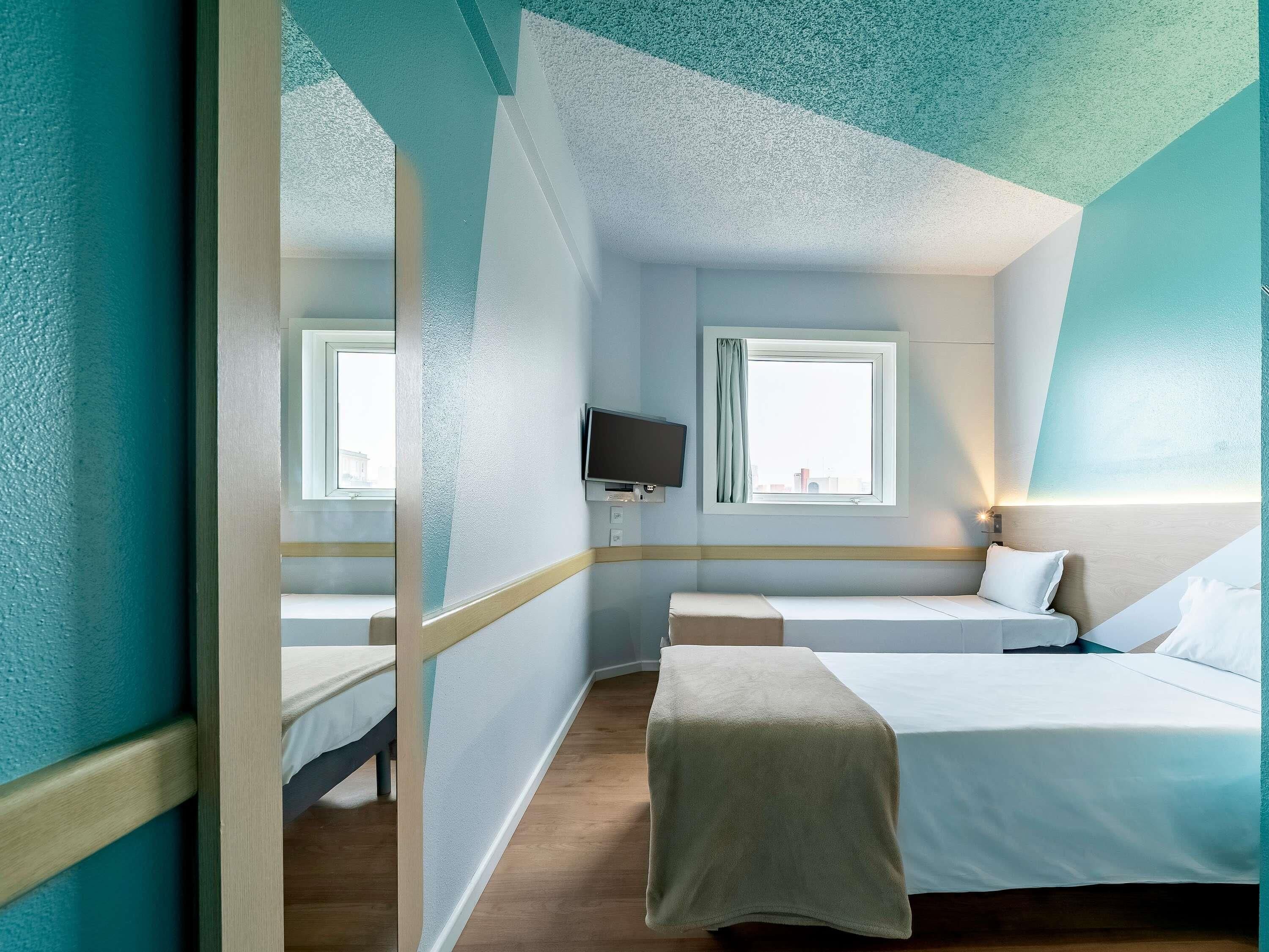 Habitación de hotel con cama, televisión, ventana con cortinas y vista a la ciudad.