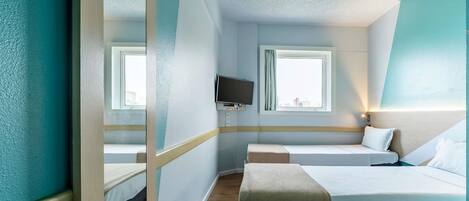 Habitación de hotel con cama, televisión, ventana con cortinas y vista a la ciudad.