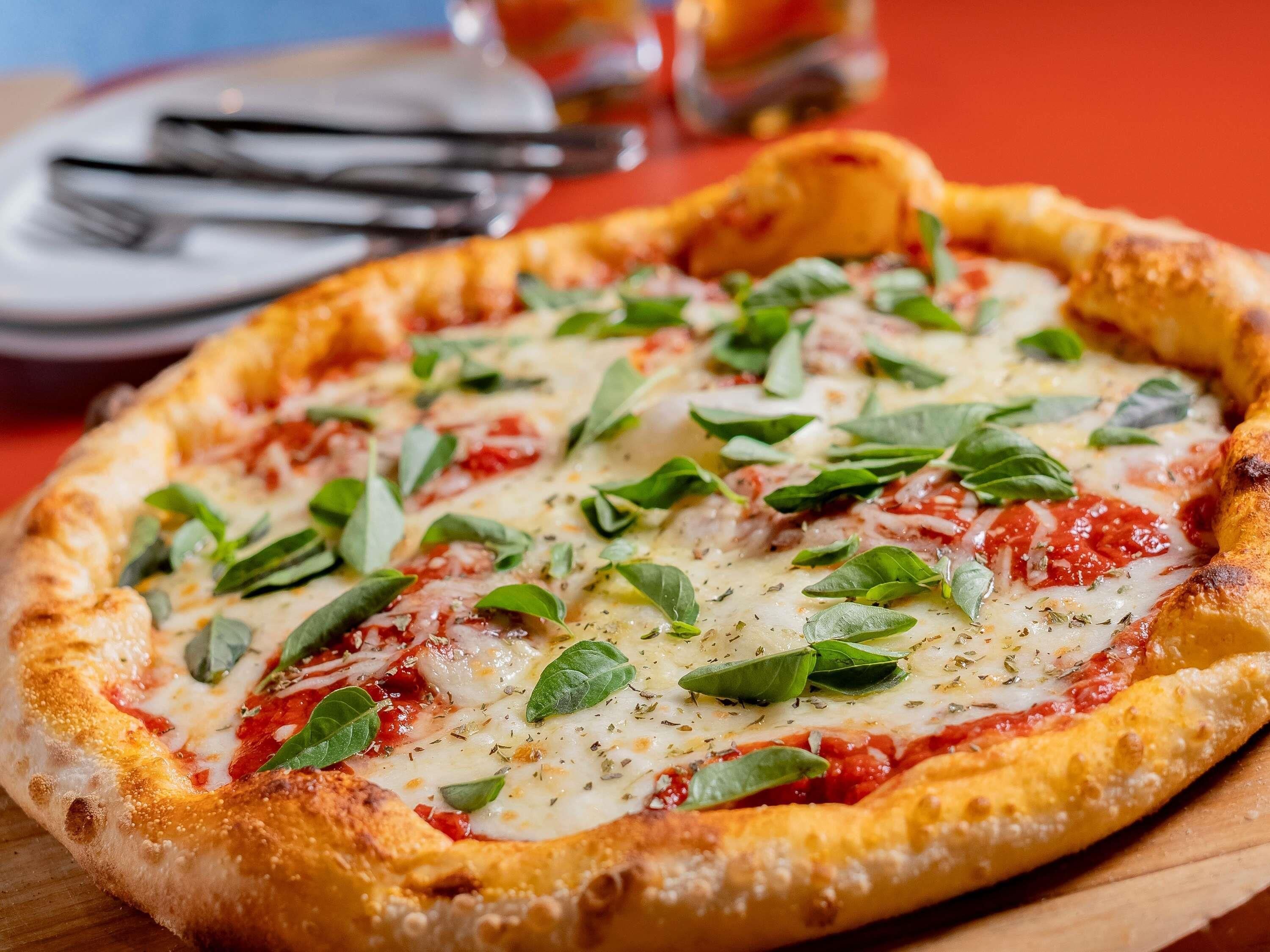 Pizza com massa grossa, coberta com queijo, manjericão e molho de tomate.