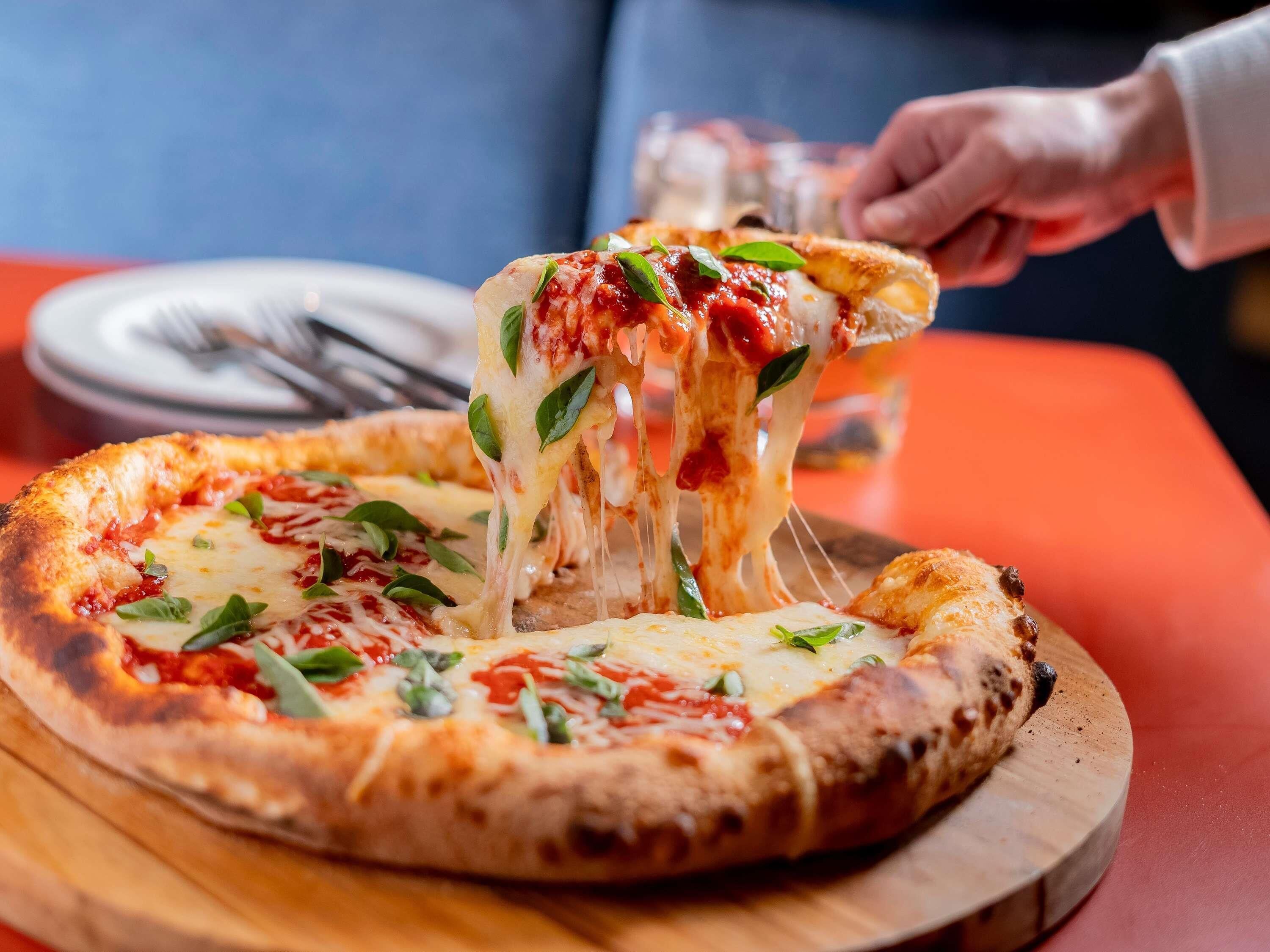 A pizza with a golden-brown crust, cheese, and basil leaves on a wooden board.