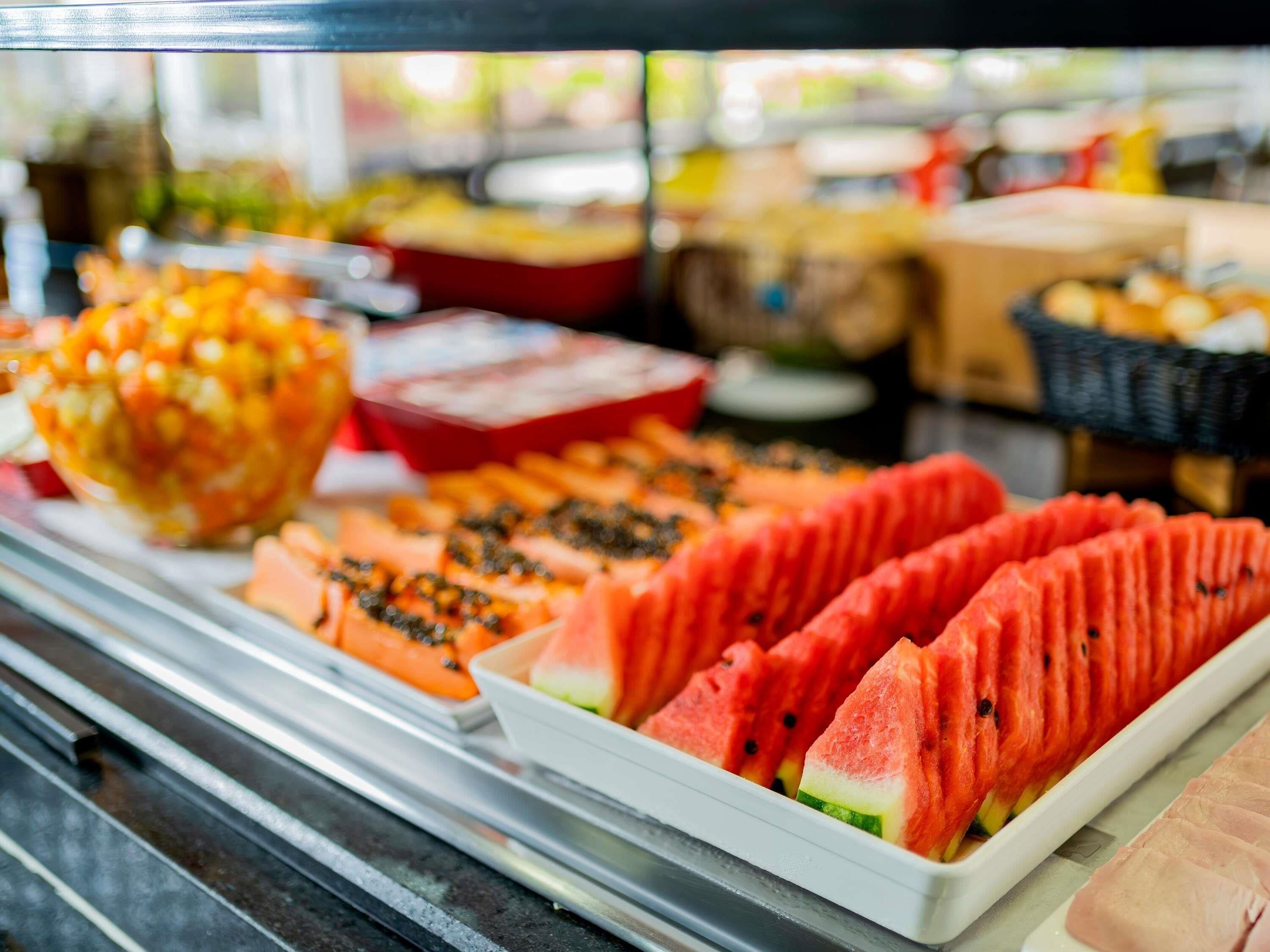 Vitrine com diversos alimentos, incluindo fatias de melancia e uma tigela que parece ser de salada de frutas.