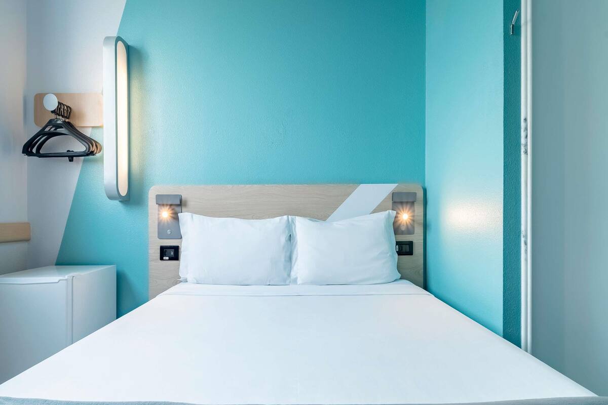 Una habitación de hotel moderna con cama, lámparas de noche, una luz empotrada en la pared y un cabecero de madera.