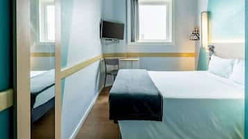 Quarto de hotel com cama, escrivaninha, cadeira, televisão e janela.