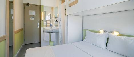 Quarto de hotel com cama, banheiro com pia e espelho, e uma porta.